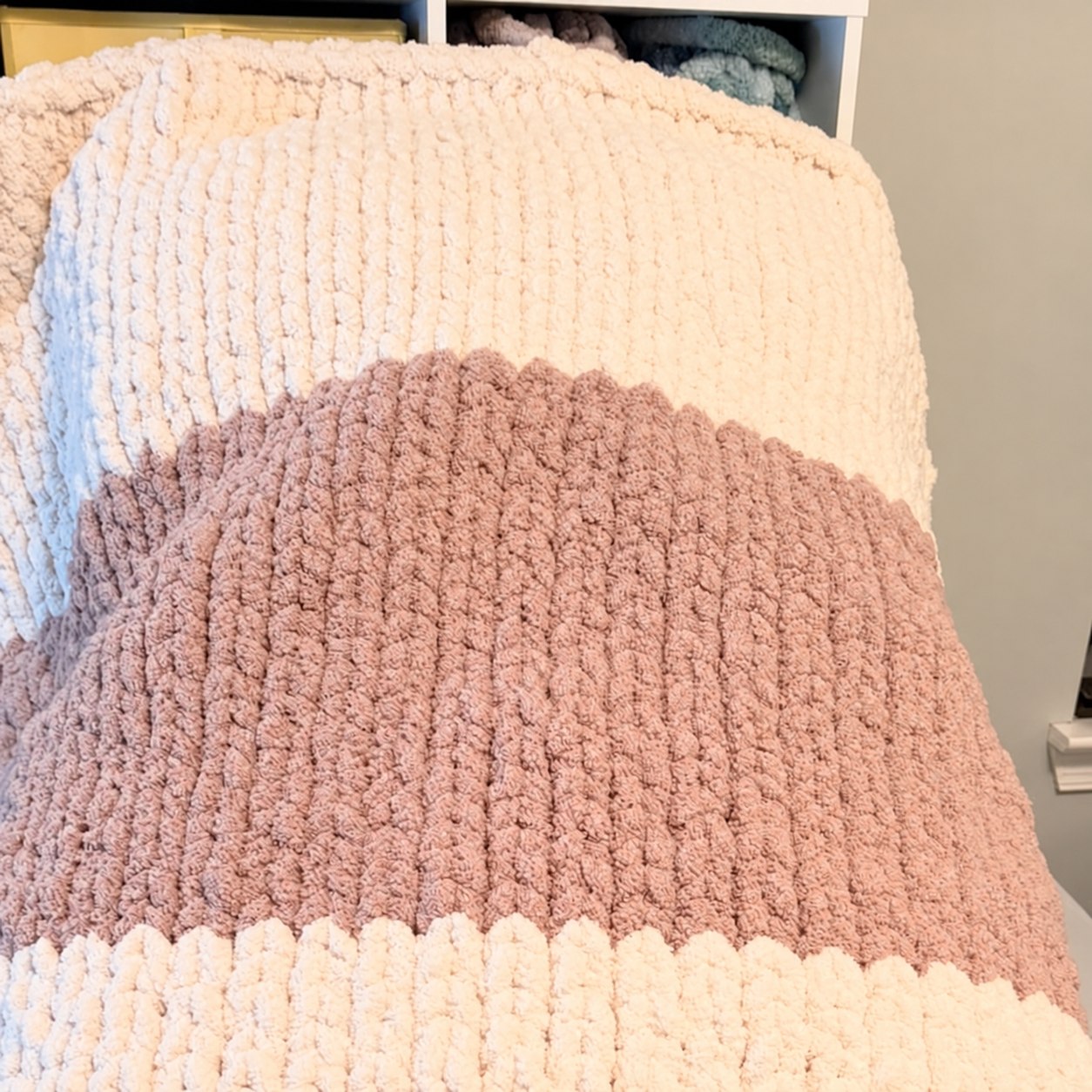 Chunky knit blanket with cream and dusty rose stripes draped over a chair